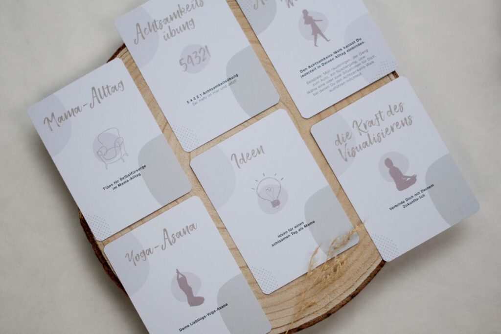 Verschiedene Achtsamkeitskarten für Mütter liegen lesbar auf einer Holzscheibe